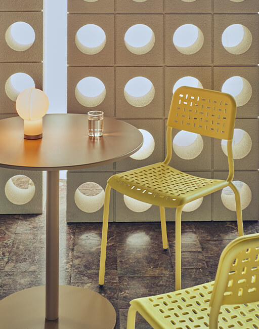 Perforowane krzesła tworzywowe Tube w kolorze żółtym przy okrągłym stole na tle rzeźbiarskiej ściany