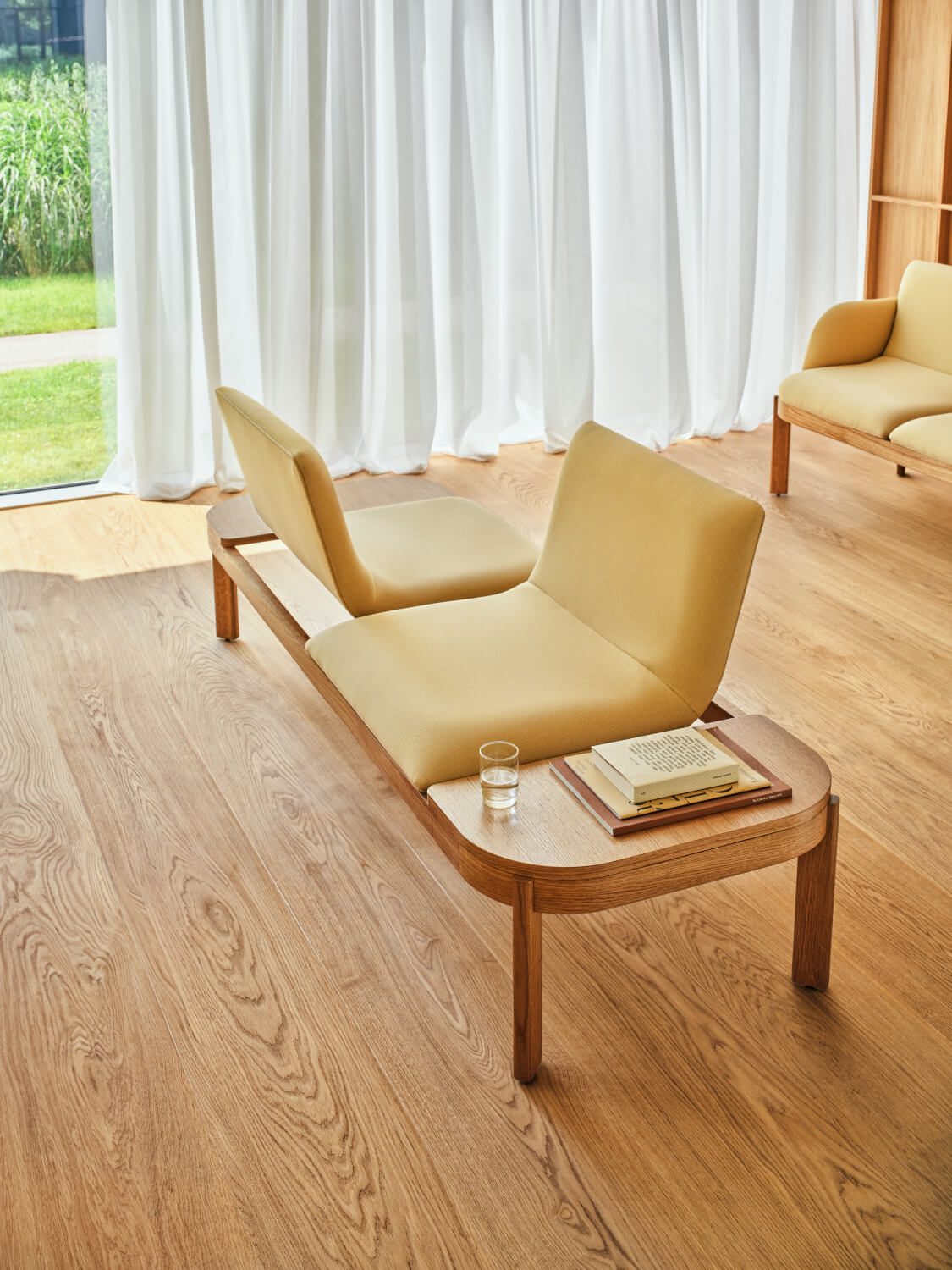 Jasnożółta sofa na drewnianej podstawie z siedziskami skierowanymi w przeciwne strony