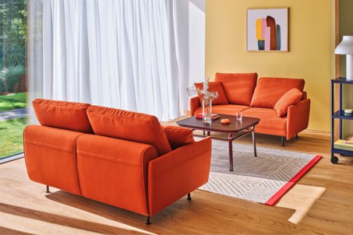 Jasnoszara sofa narożna z miękkimi poduszkami oparciowymi i smukłymi metalowymi nogami