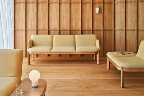 Trzyosobowa sofa w beżowej tapicerce z widoczną drewnianą ramą